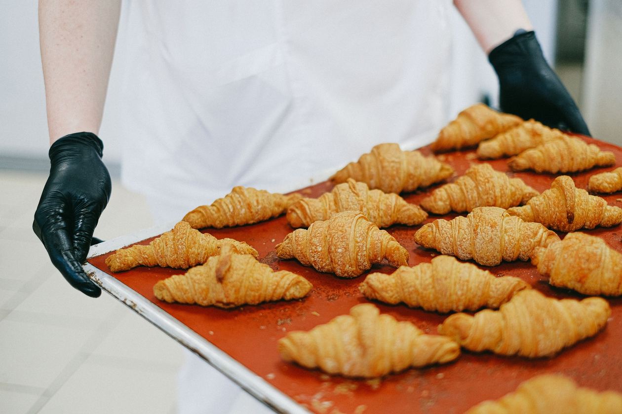 Plaque de croissants dorés tenue par des mains gantées.