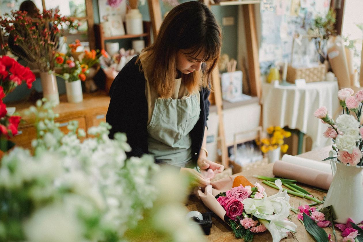 Fleuriste préparant l’emballage d’un bouquet sur un plan de travail.