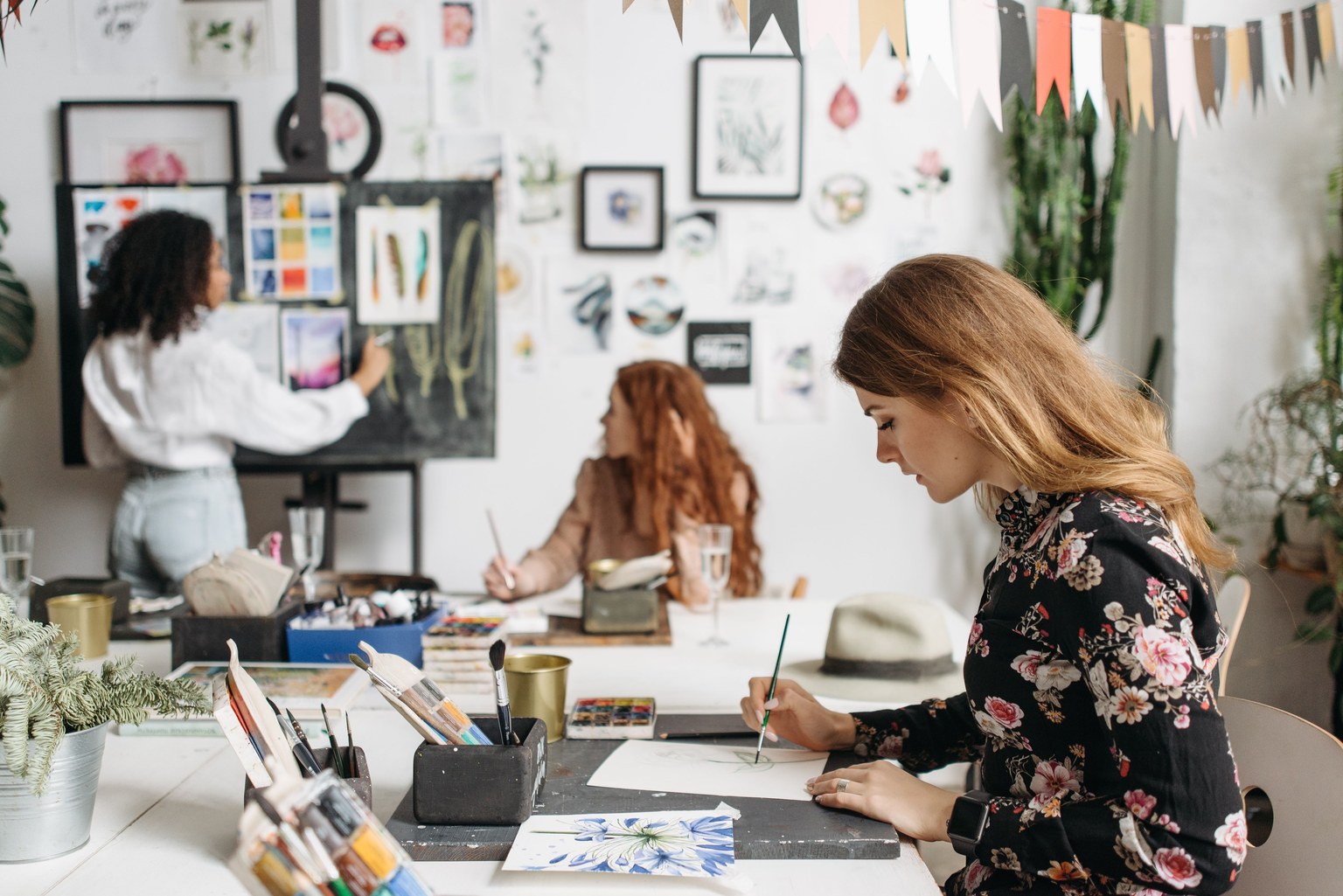 Trois femmes participant à un atelier de peinture autour de tables dans une salle lumineuse.