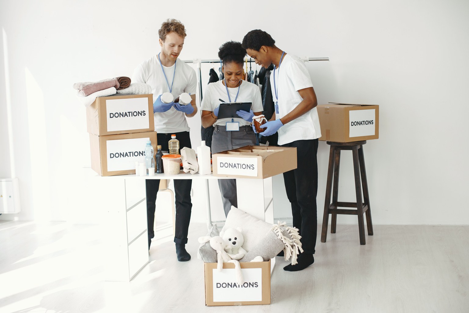 Trois adultes organisant des cartons de dons dans une pièce lumineuse.