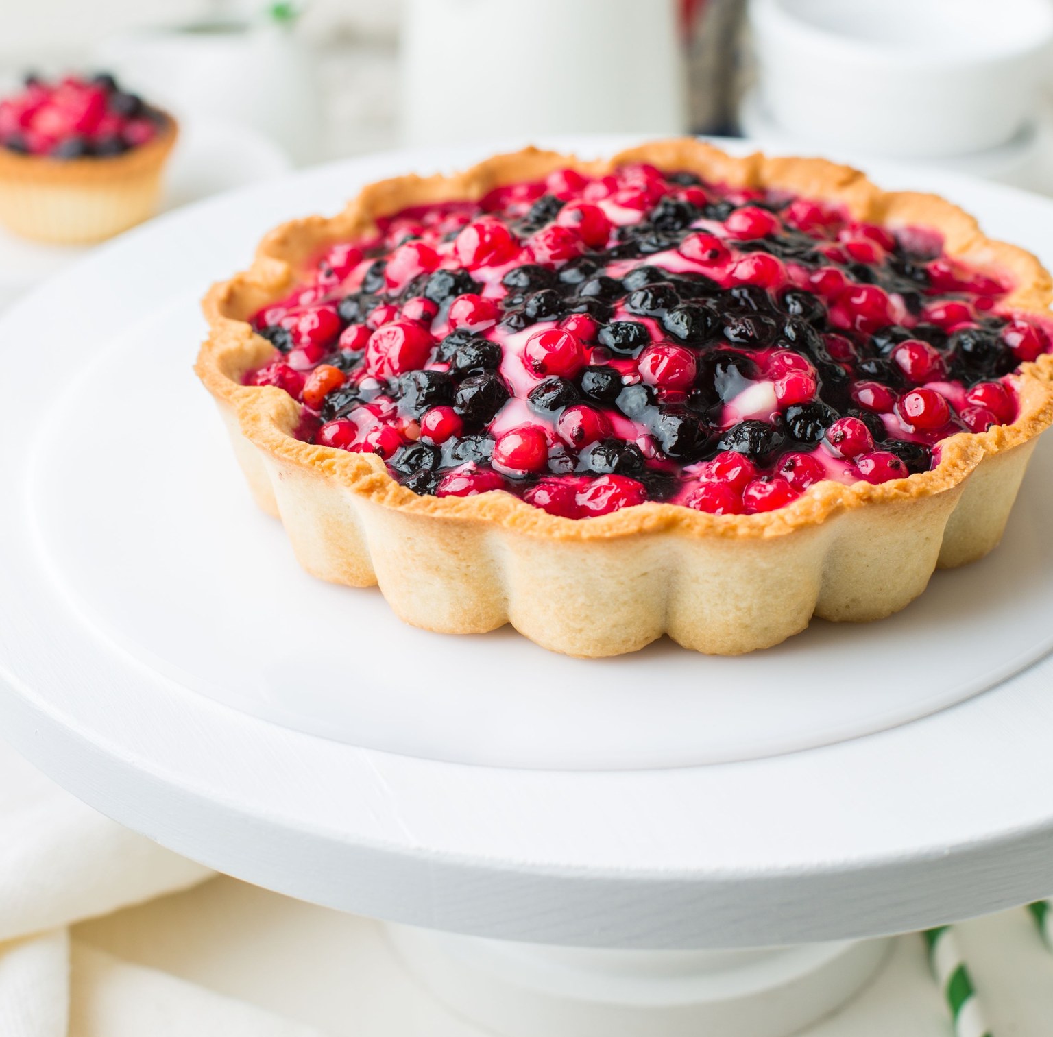 Tarte garnie de baies rouges et noires sur un présentoir blanc.