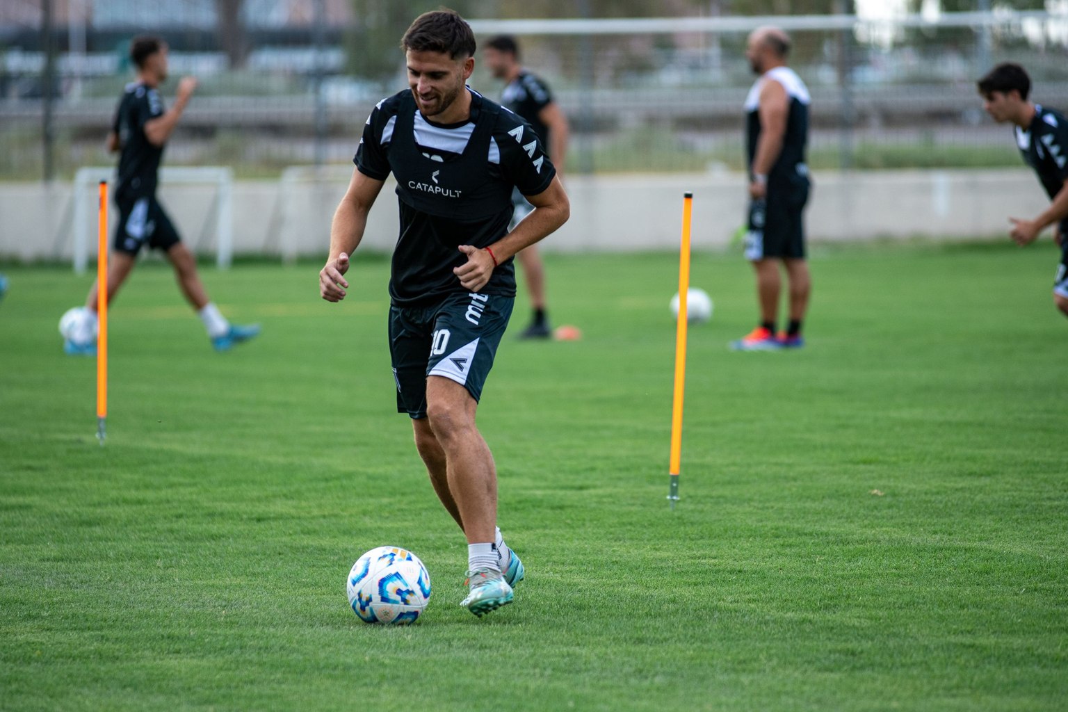 Footballeur conduisant un ballon sur une pelouse entre des piquets d’entraînement.