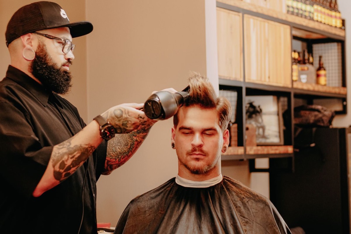 Coiffeur barbier séchant les cheveux d'un client homme dans le salon mixte