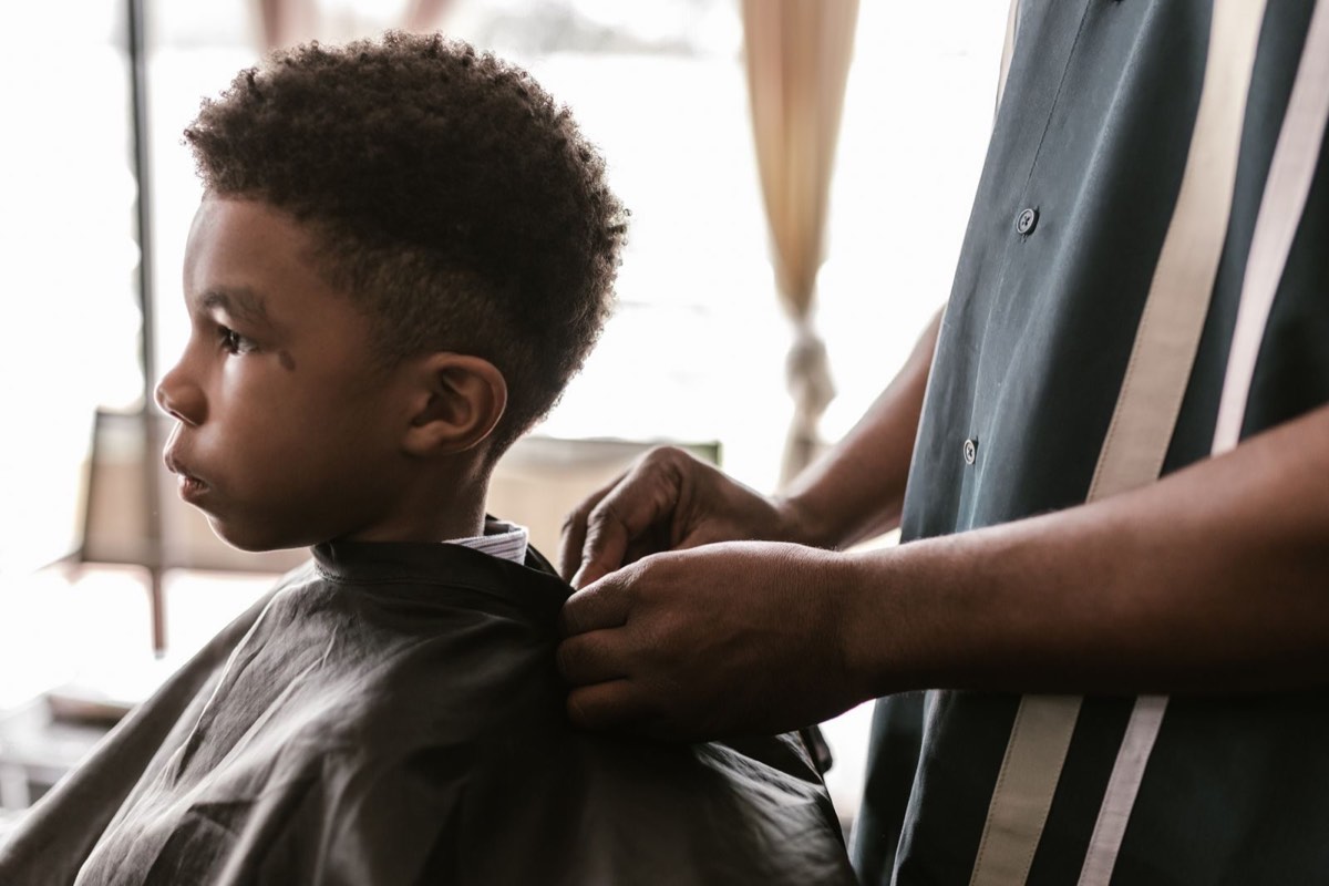 Enfant en cape assis chez le coiffeur, vu de profil