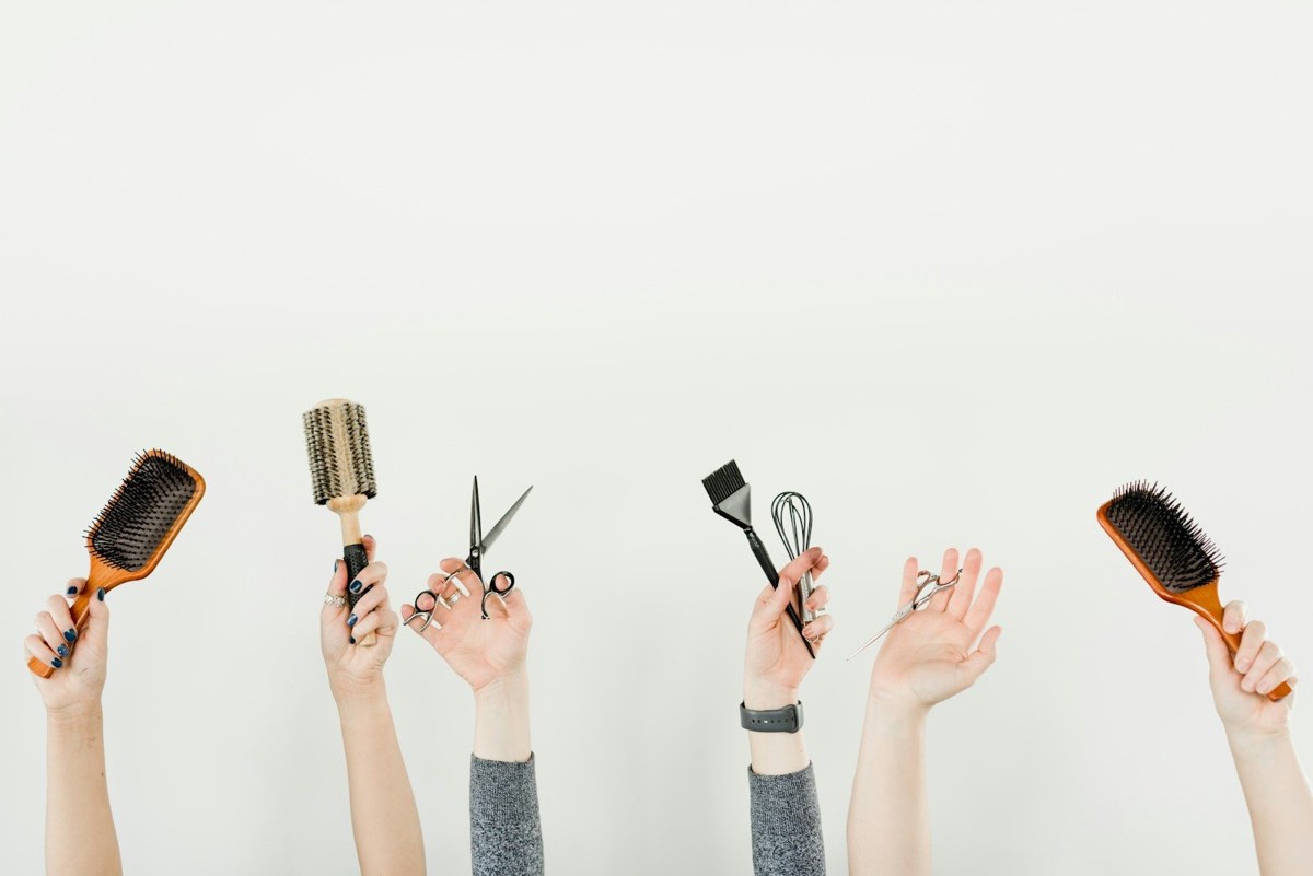 Mains de l'équipe tenant ciseaux, peignes et brosses du salon