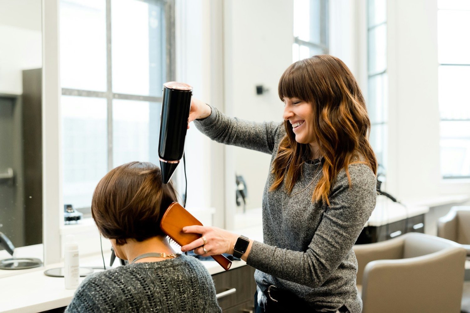 Coiffeuse souriante réalisant un brushing dans la salle du salon Coiffure des Halles