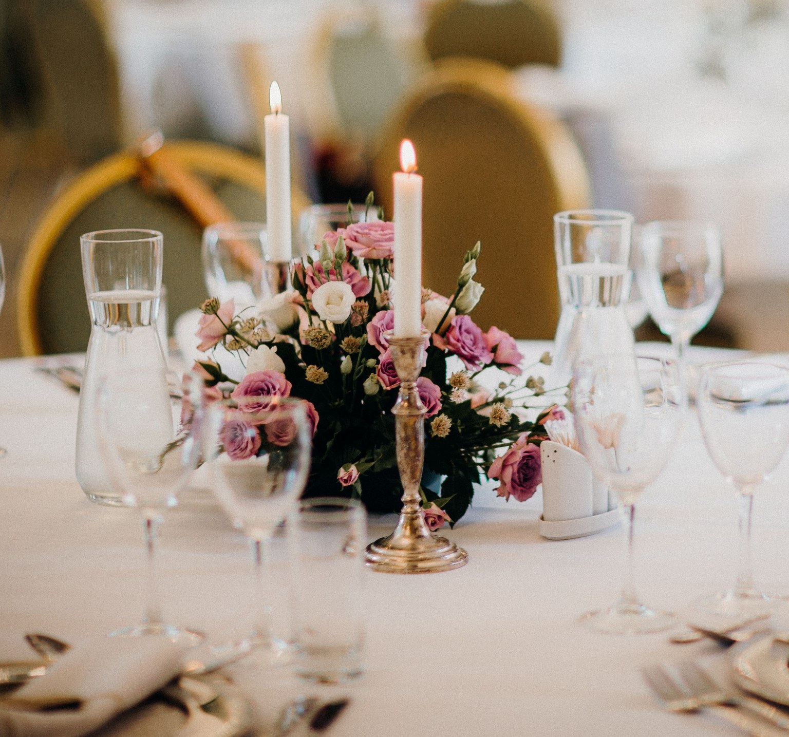 Composition de fleurs roses et blanches entre des bougies sur une table de réception.