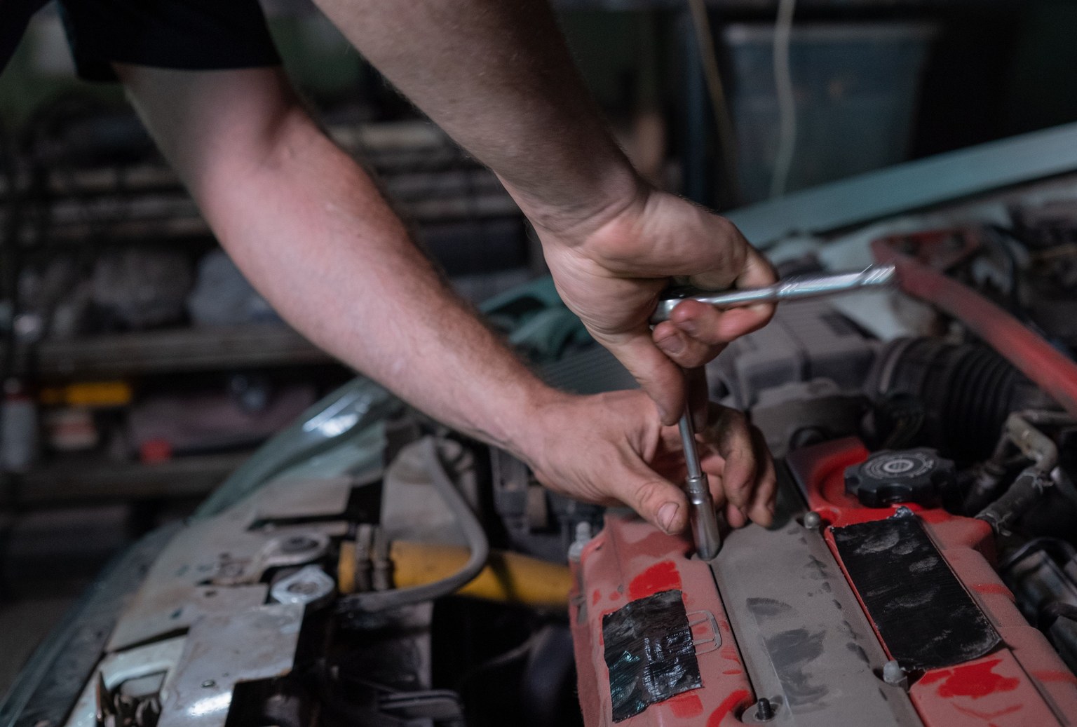 Mains utilisant une clé à cliquet et une douille sur un moteur sous un capot ouvert.