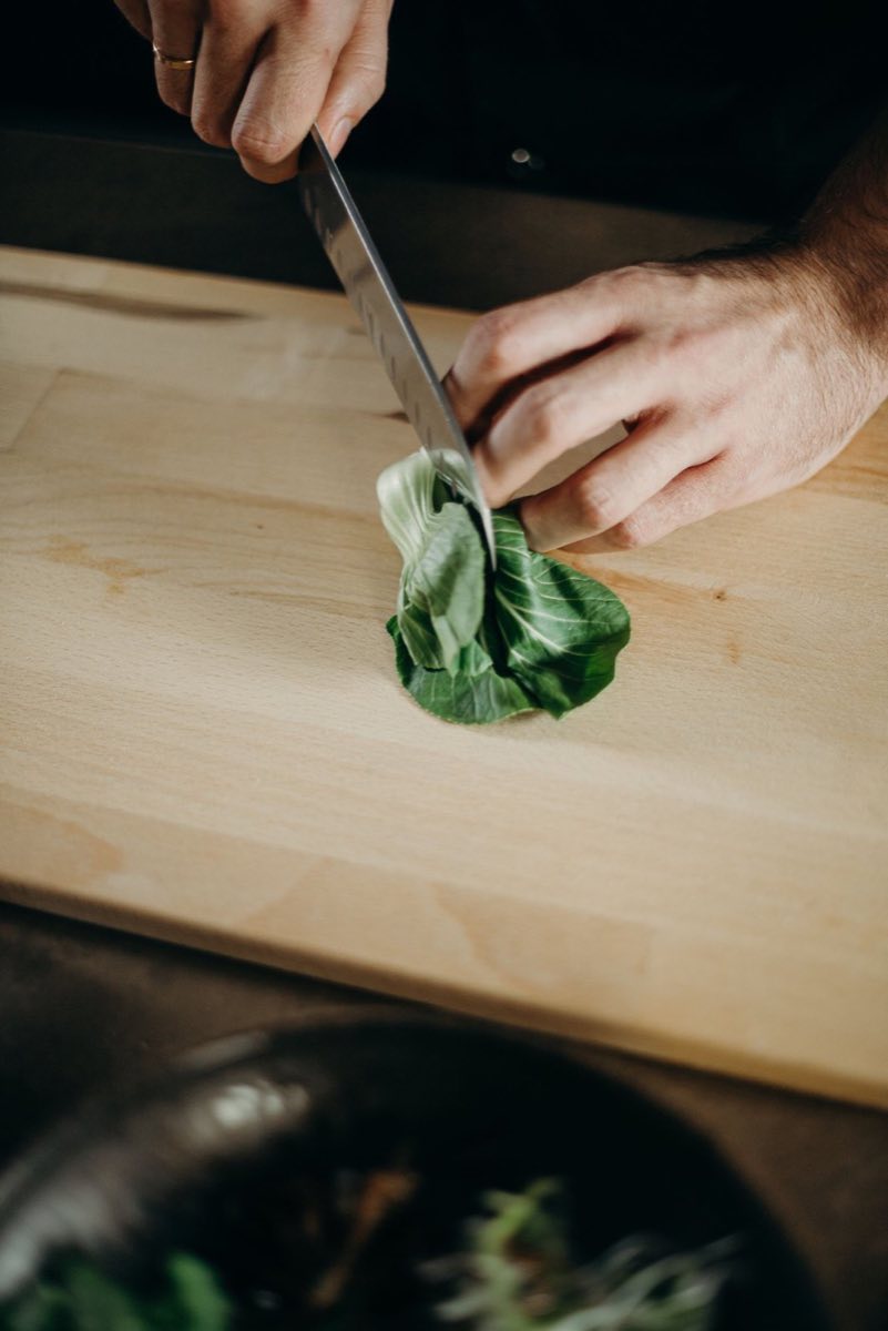 Légumes taillés au couteau en cuisine, sur une planche en bois clair