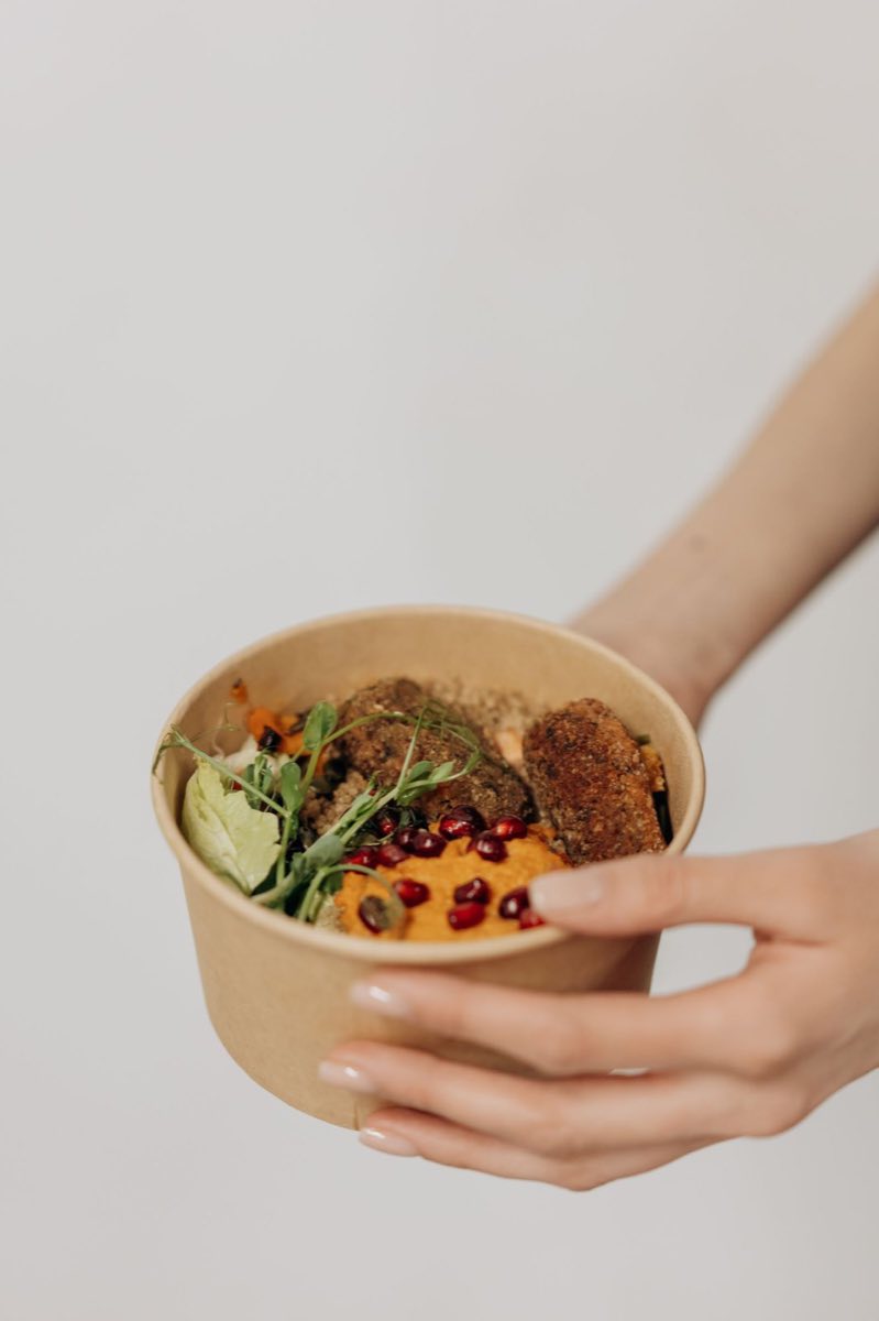 Plat à emporter tenu à la main dans un bol carton kraft : falafels, houmous de carotte, quinoa et grenade