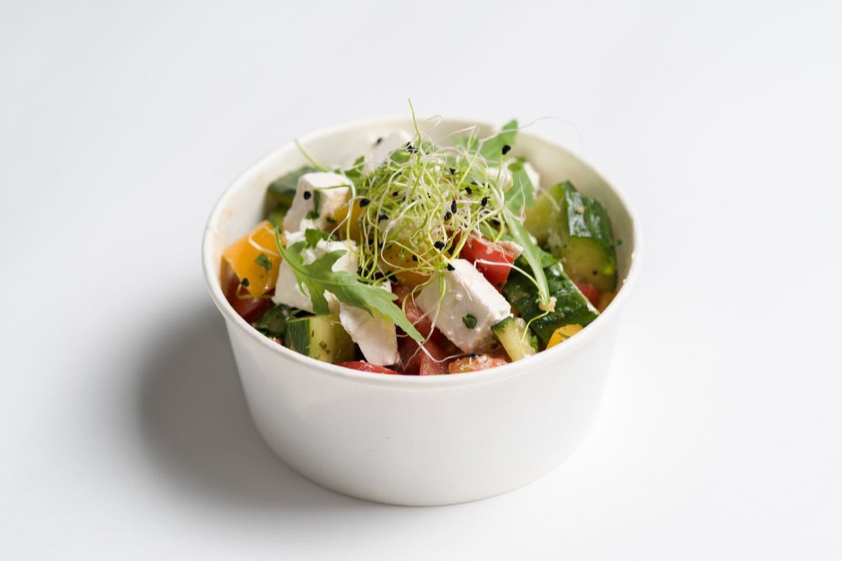 Salade composée servie dans un bol blanc : concombre, tomate, pousses et graines