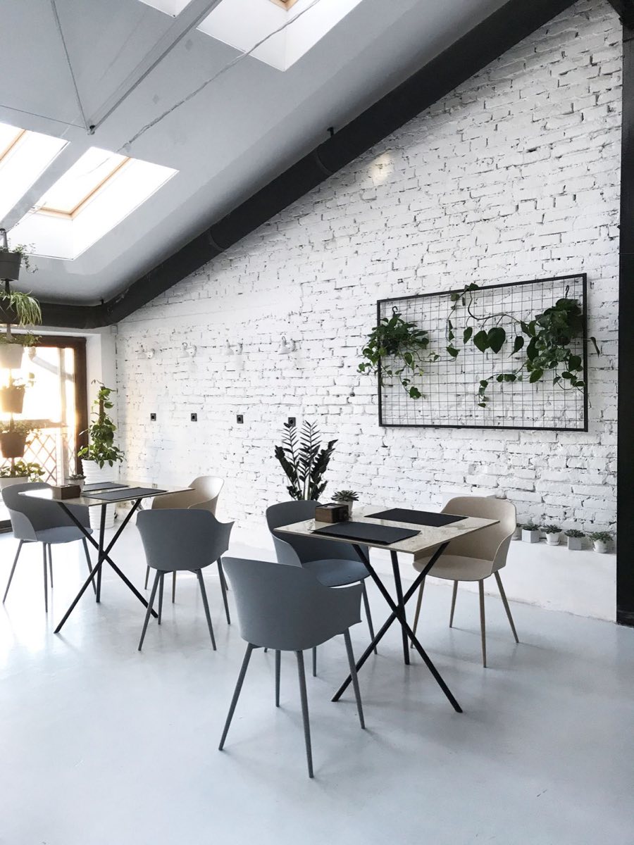 Salle claire de la cantine, mur de brique blanche, plantes vertes et mobilier contemporain