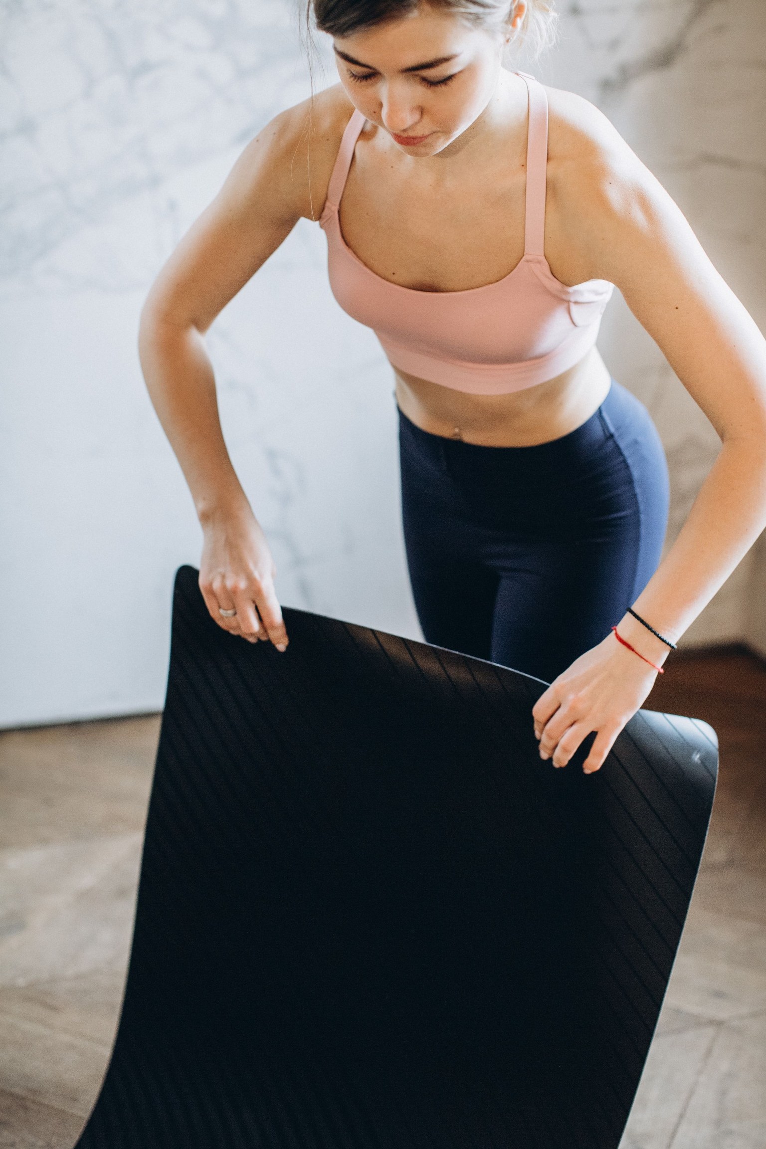 Femme déroulant un tapis de yoga sur un parquet dans une pièce lumineuse.